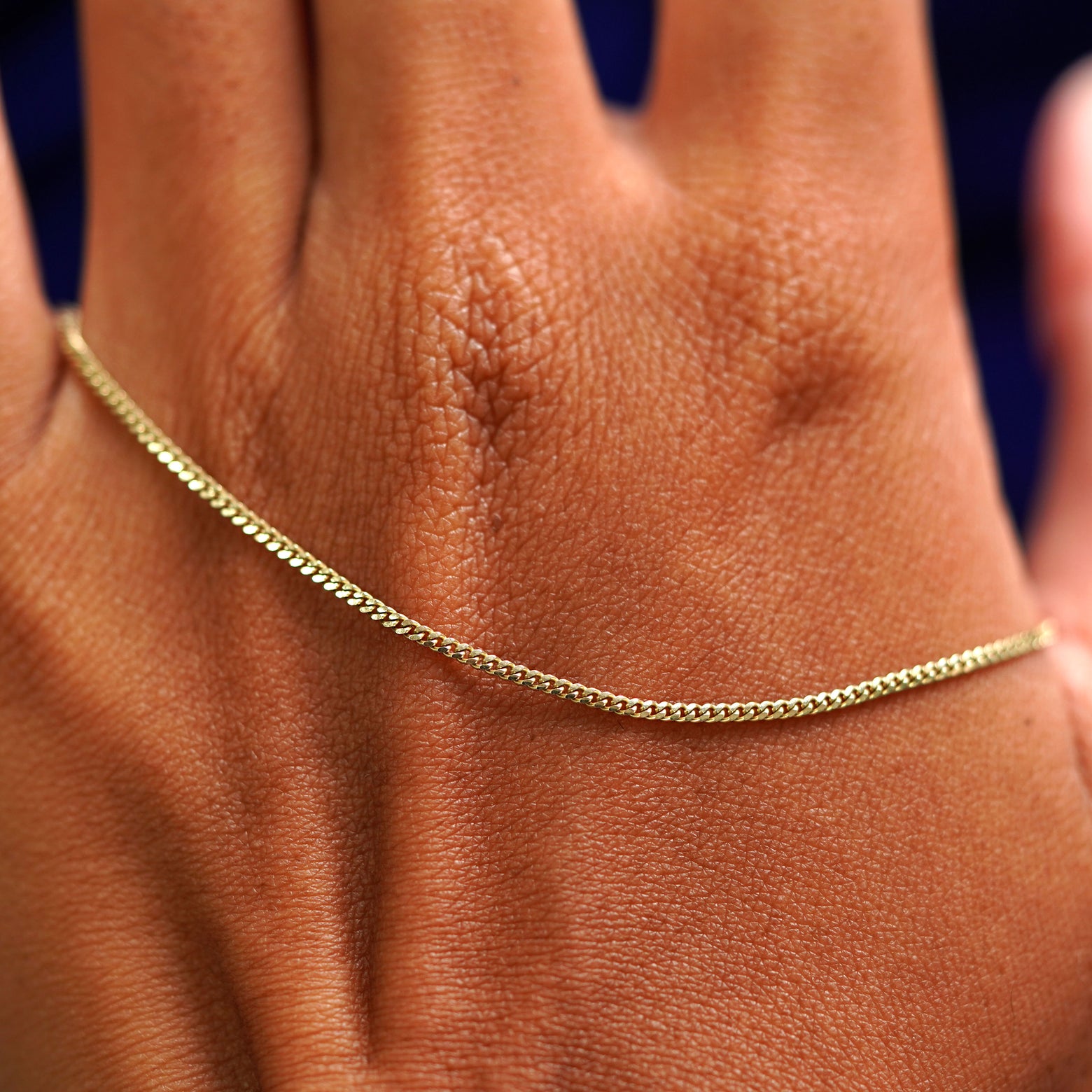 A solid gold Mini Miami Chain resting on the back of a model's hand