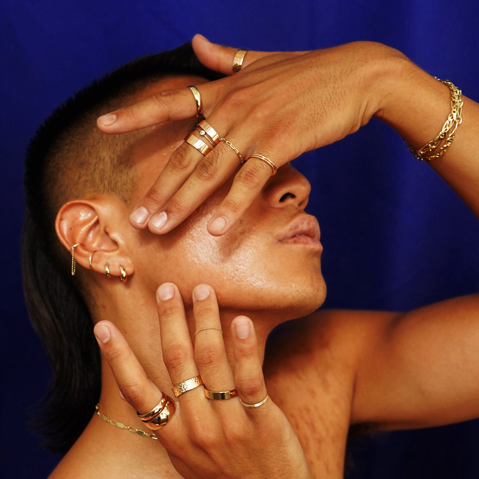 A model with head tilted up and their hands raised over their face wearing various Automic Gold jewelry