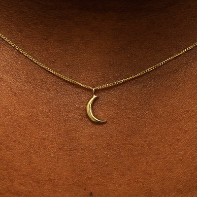 Close up view of a model's neck wearing a 14 karat gold crescent moon necklace