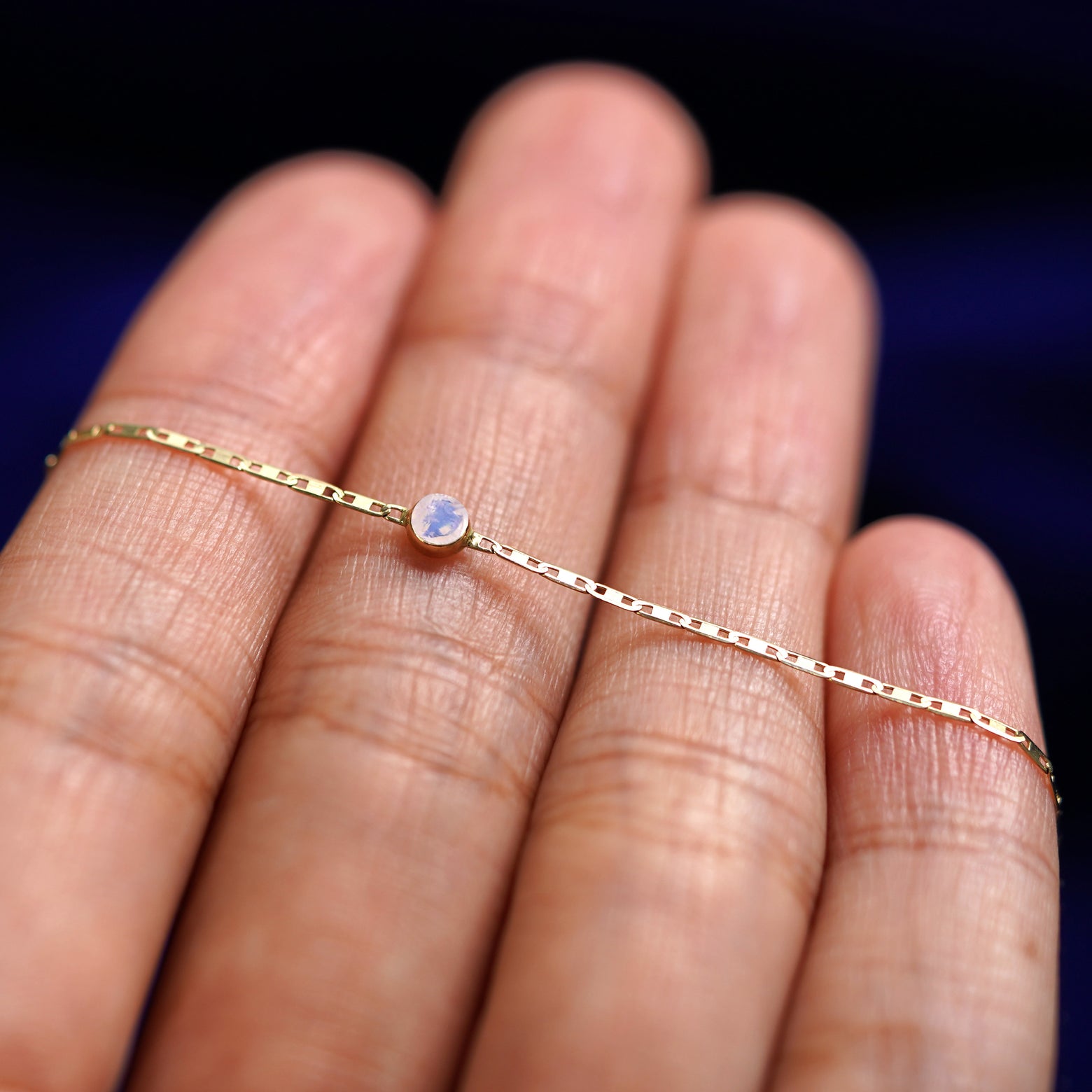 A yellow gold Moonstone Bracelet resting on a model's fingers