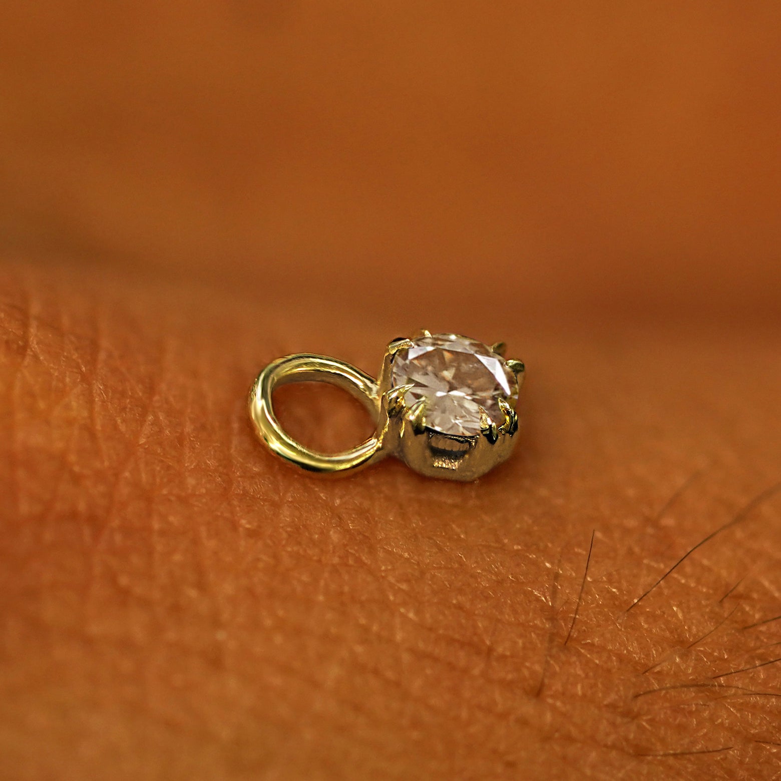A solid yellow gold Champagne Diamond Charm for earring resting on the back of a model's hand
