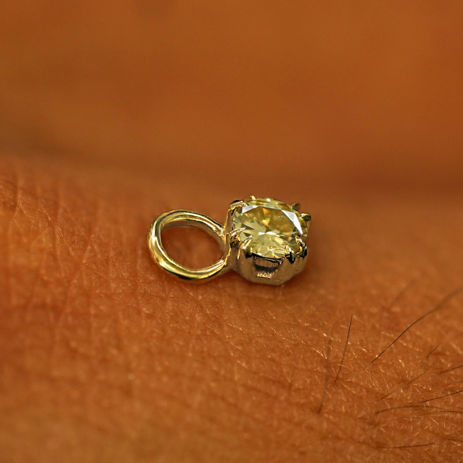 A solid yellow gold Champagne Diamond Charm for earring resting on the back of a model's hand