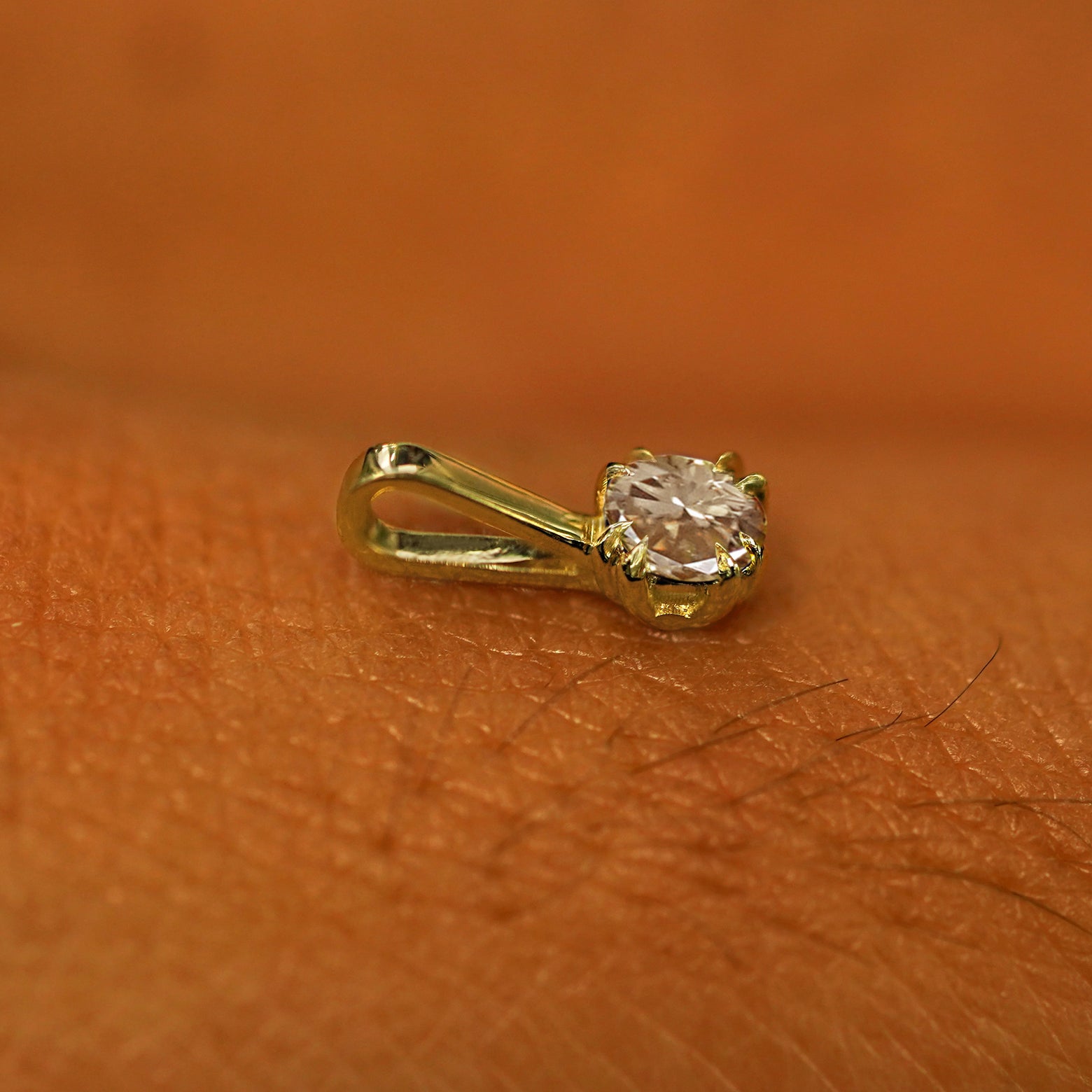 A 14k yellow gold Champagne Diamond Charm for chain resting on the back of a model's hand