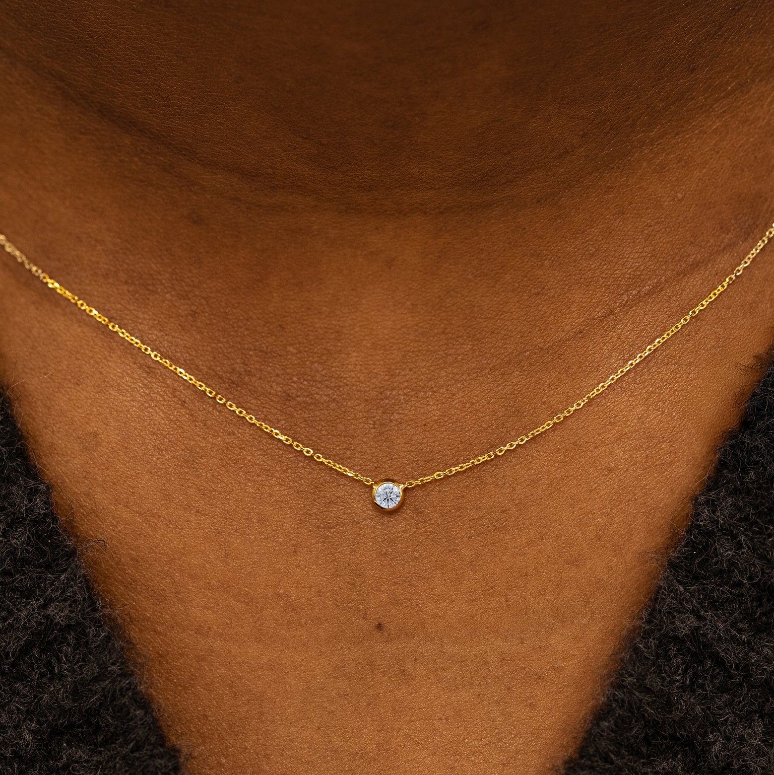 Close up view of a model neck wearing a 14k yellow gold Bezel set Natural Diamond gemstone necklace 
