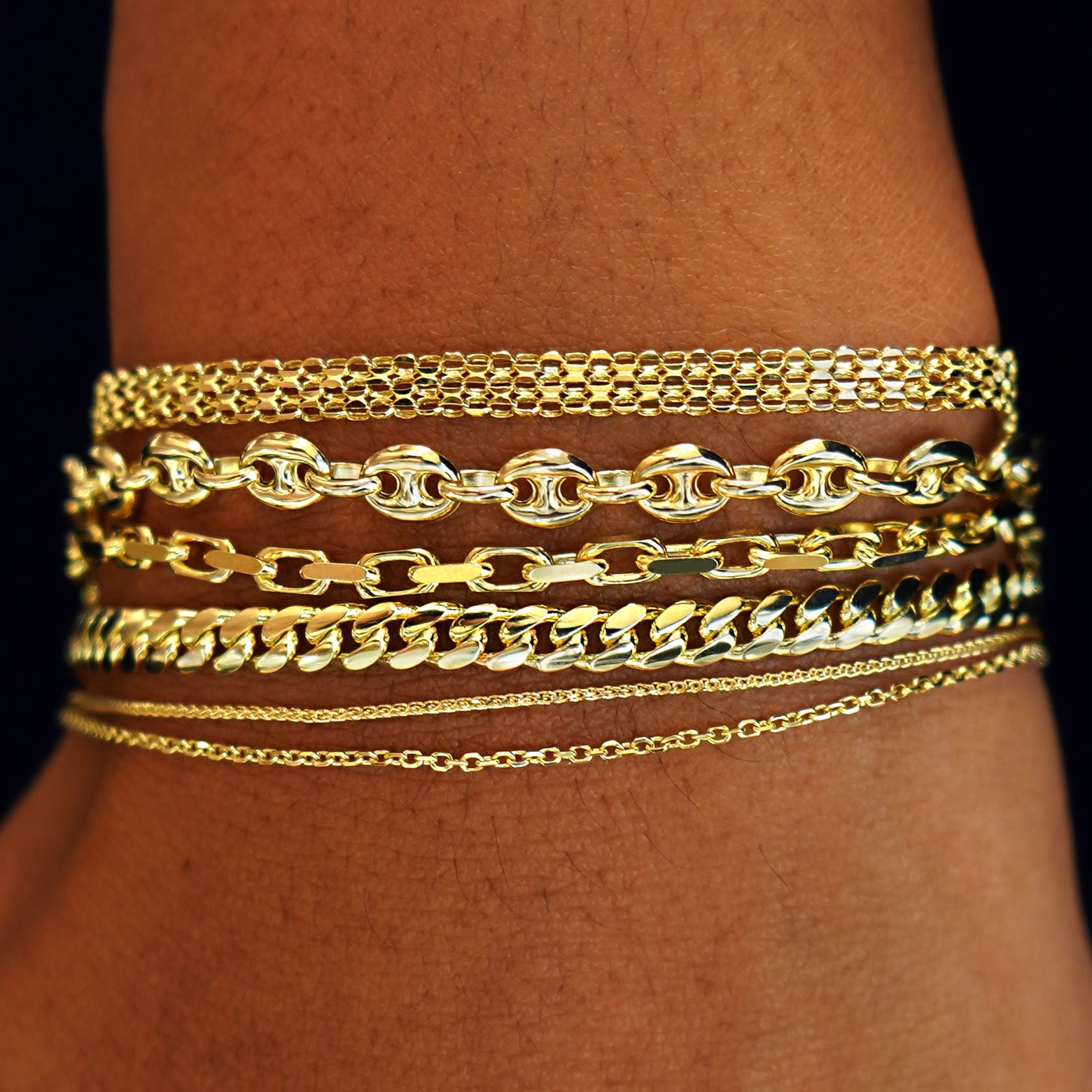 A model's wrist wearing yellow gold Bismarck, Anchor, Anchor, Medium Miami, Wheat, and Medium Cable Bracelets