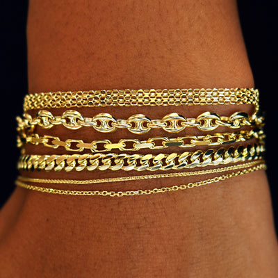 A  model's wrist wearing  yellow gold Bismarck, Puffy Mariner, Anchor, Medium Miami, Wheat, and Medium Cable Bracelets