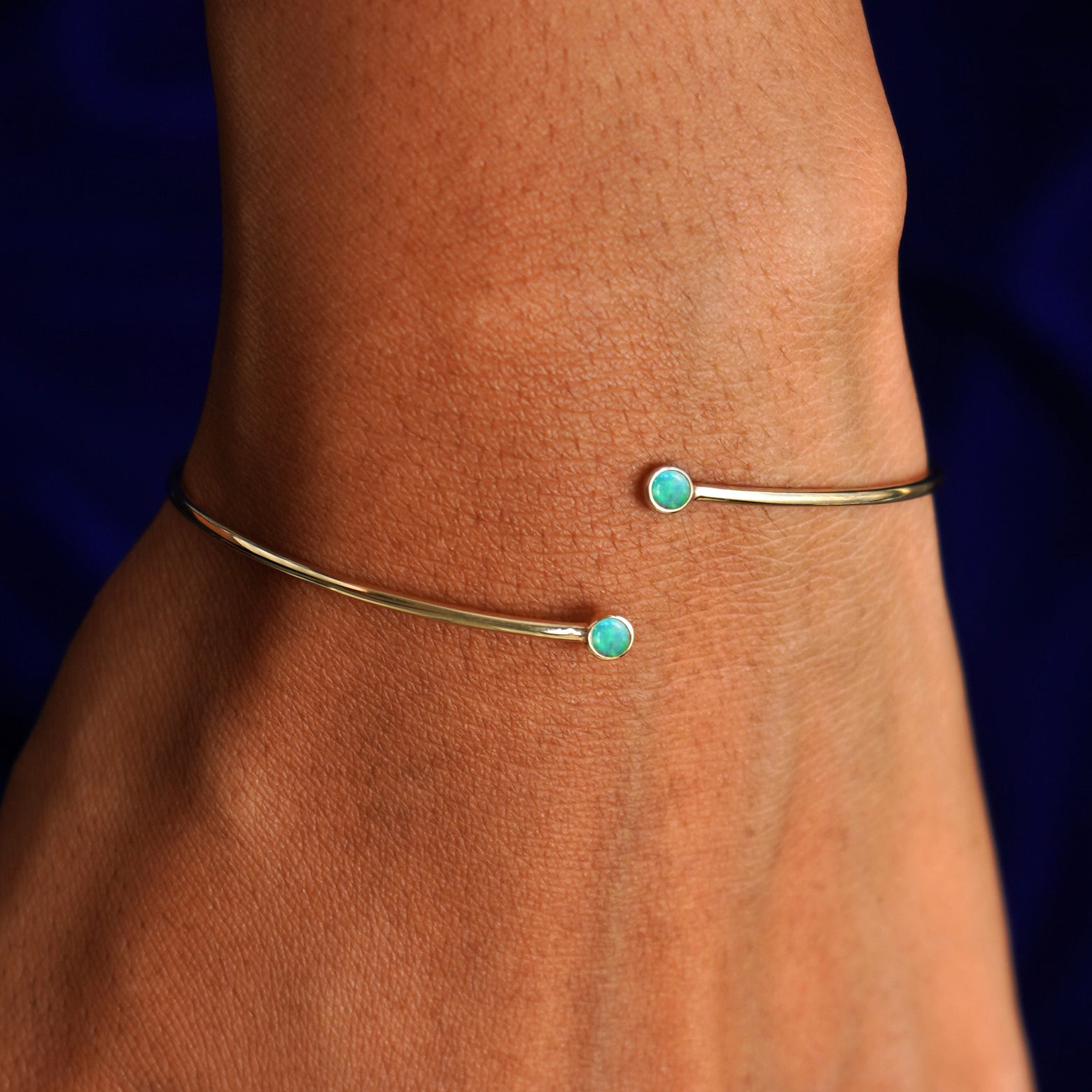 Close up view of a model's wrist wearing a 14k gold opal gemstone bypass bangle