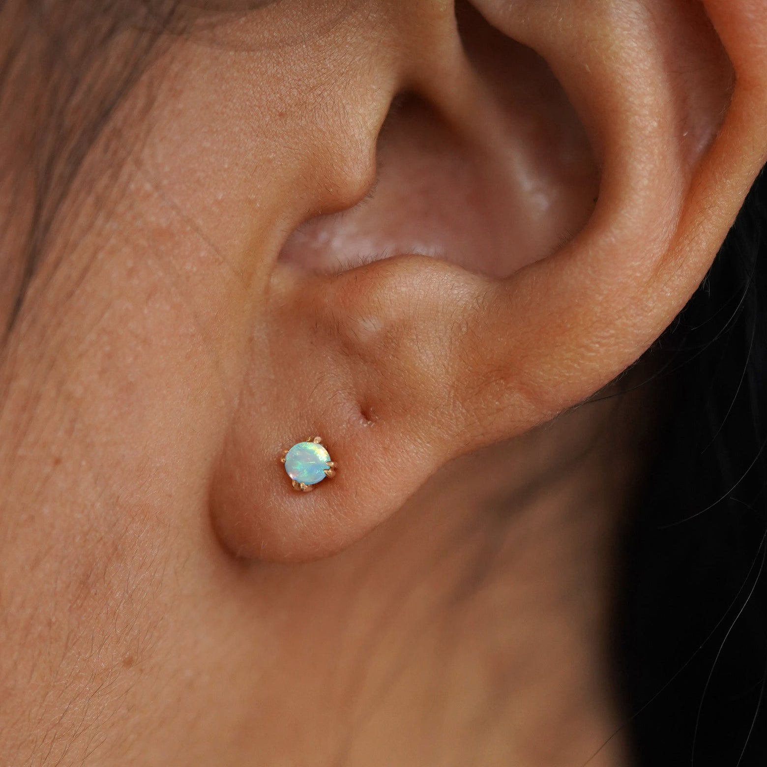 Close up view of a model's ear wearing a 14k yellow gold Opal Earring