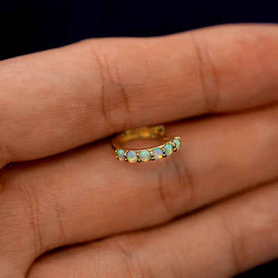 A small Opal huggie hoop earring between a model's fingers to show the gems
