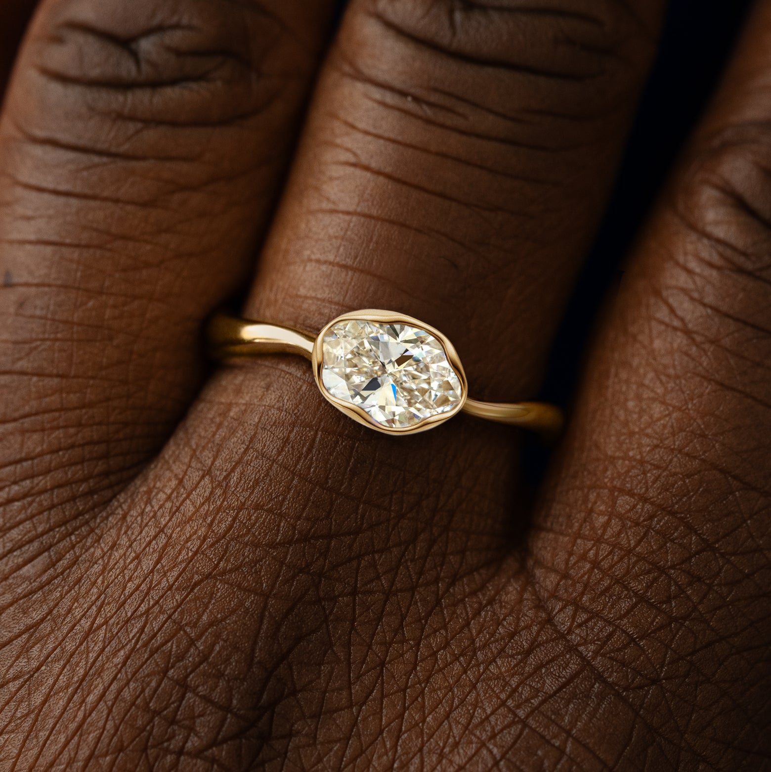 Close up view of a model's hand wearing a 14k yellow gold oval clear lab diamond liquid ring