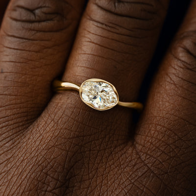 Close up view of a model's hand wearing a 14k yellow gold oval clear lab diamond liquid ring