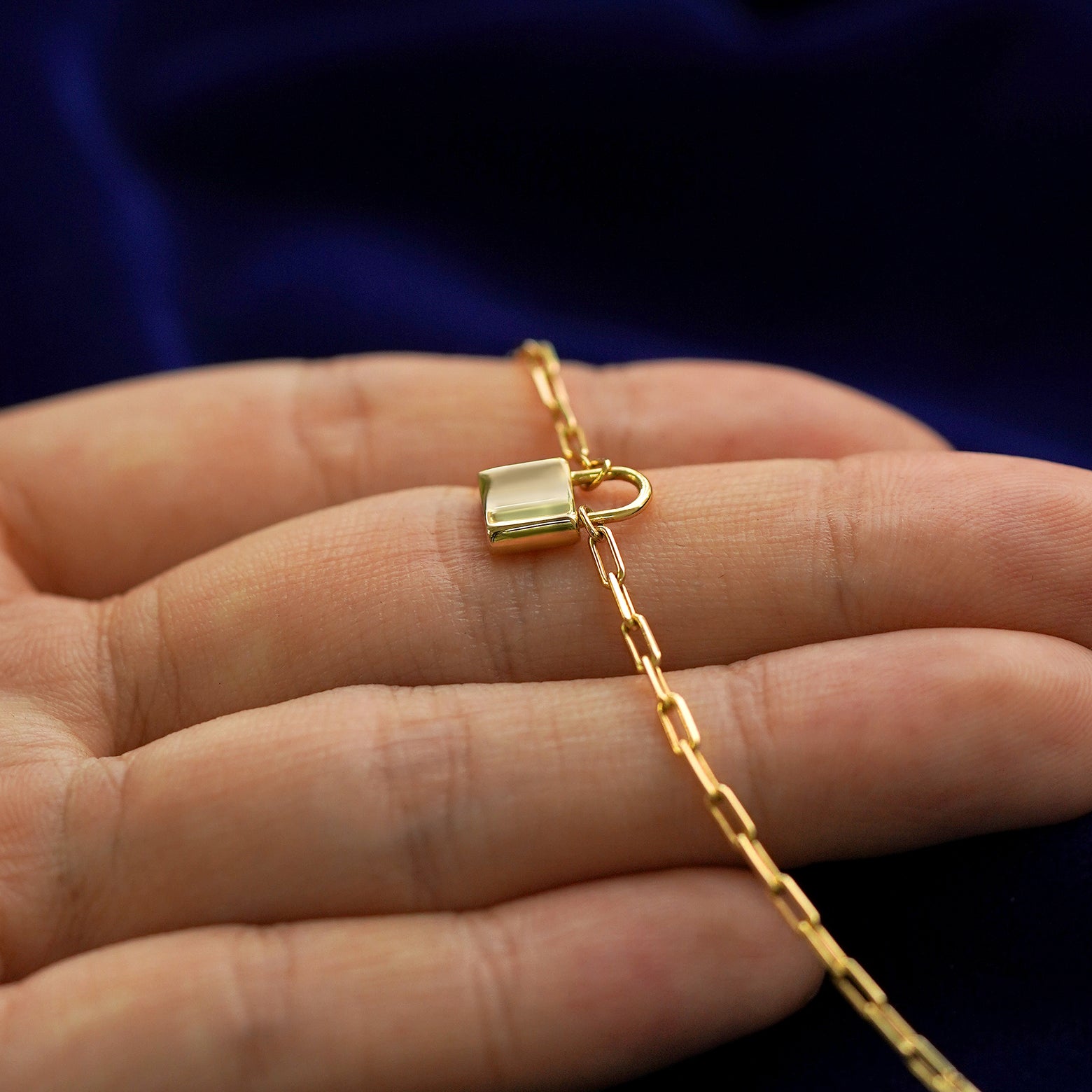 Front side view of a 14k gold padlock pendant necklace lying across a model's fingertips