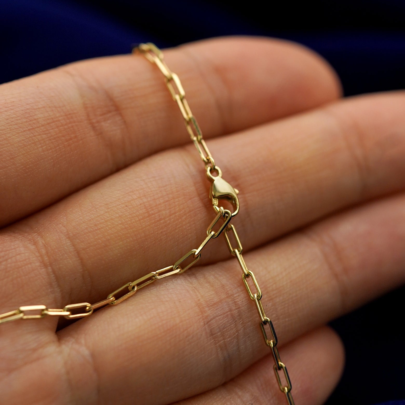 A model holding a lock necklace to show the lobster clasp fastened on a chain link to make the length shorter