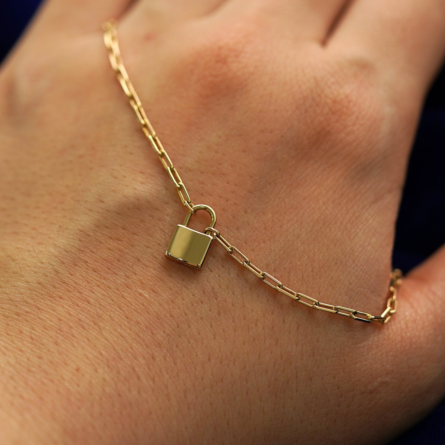 A solid gold lock necklace draped across the back of a model's hand