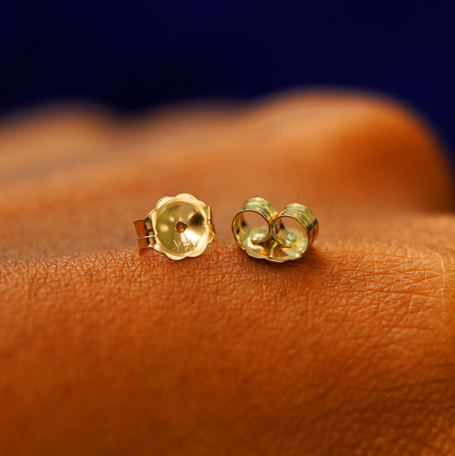A pair of solid 14k gold large push back earring backings on the back of a hand