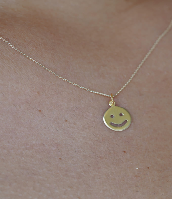 Close up view of a model's neck wearing a happy face charm on a cable chain necklace