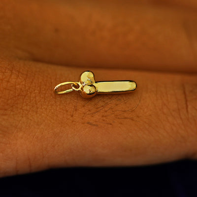 Side view of a 14k yellow gold penis charm on the back of a models finger 