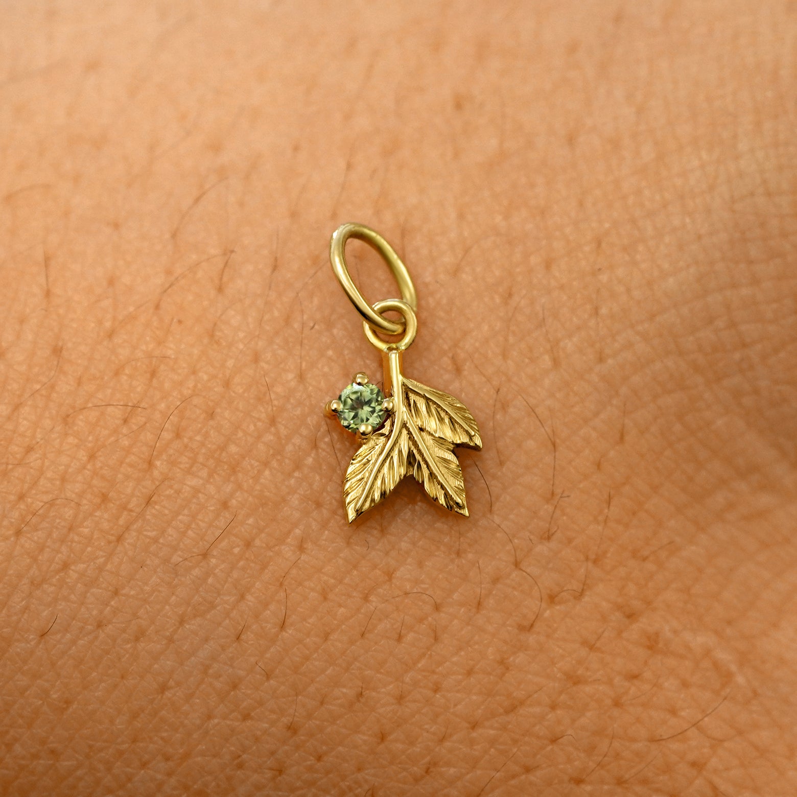 A solid 14k yellow gold peridot Gemstone 3 Leaves Charm resting on the back of a model's hand