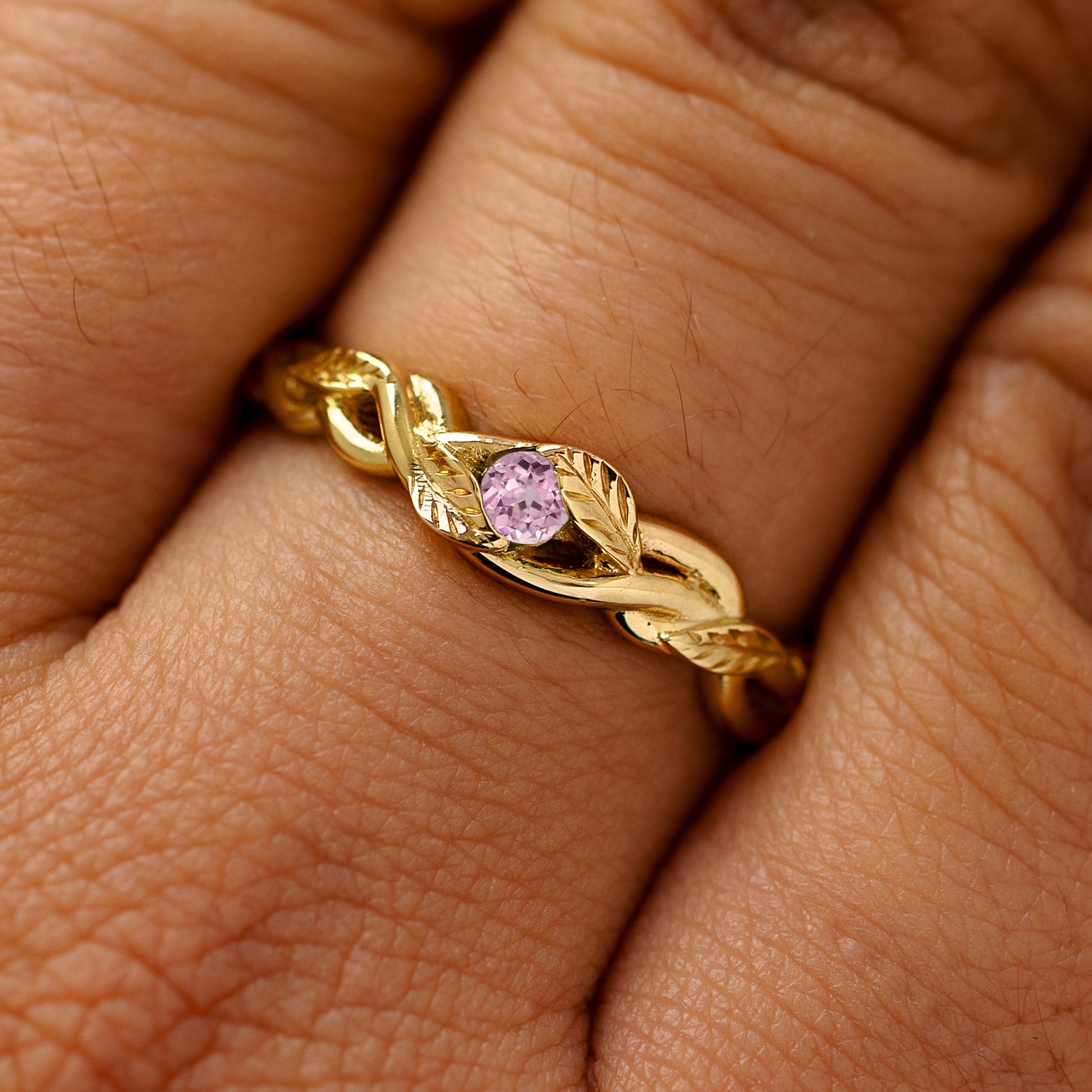 A solid 14k yellow gold pink sapphire leaves and vines ring on a model's finger