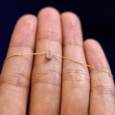 A 14k gold Pink Sapphire Necklace draped over a model's fingers