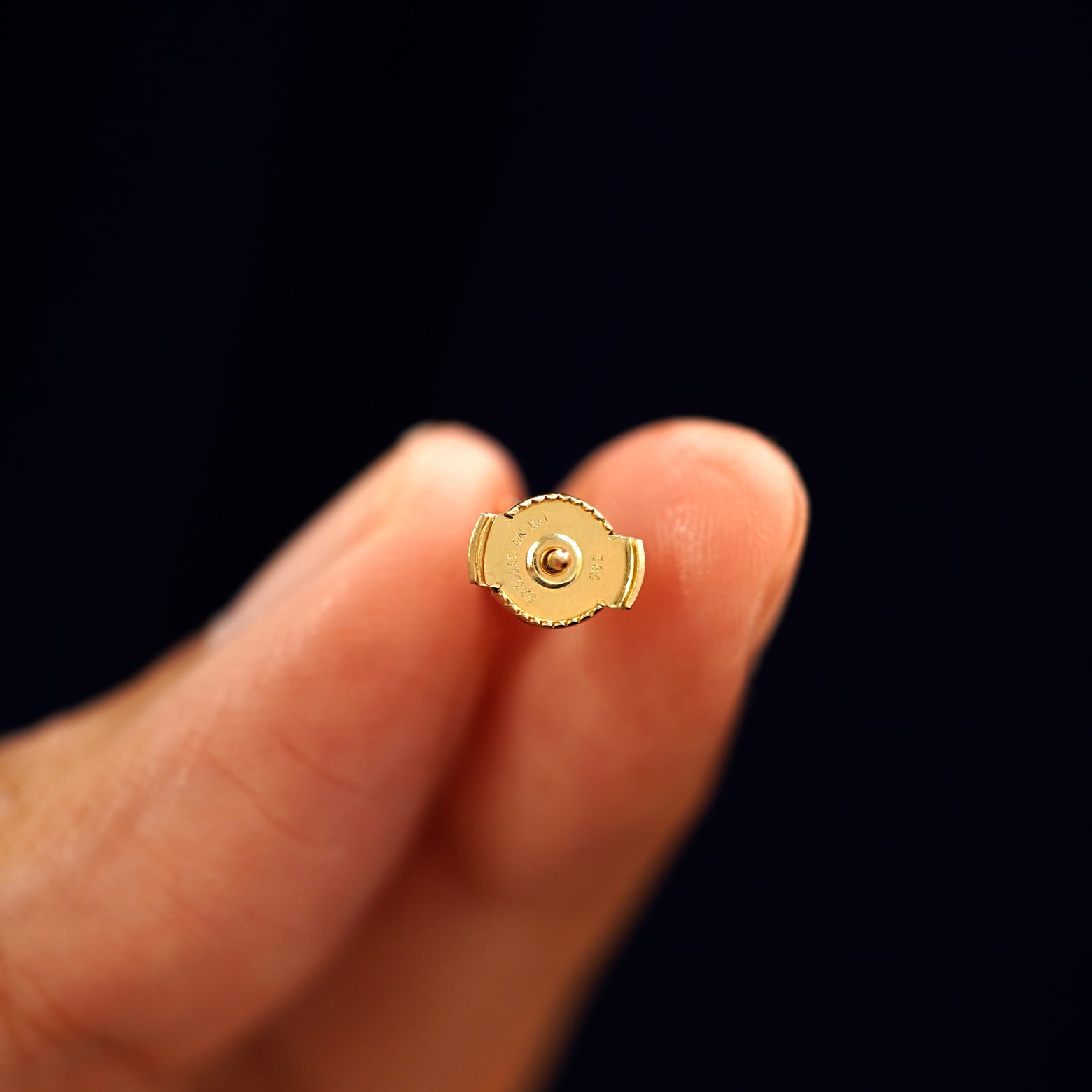 A 14k gold Blue Sapphire Pressure Lock Earring held backward between a model's fingers to show the backing