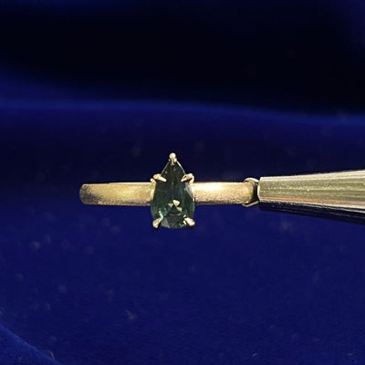 The photo displays a yellow gold matte band featuring a claw-prongs-set pear dark green sapphire.