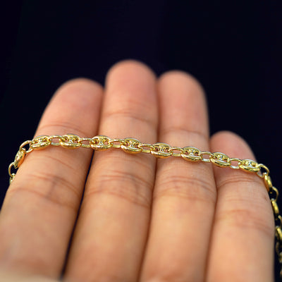 A yellow gold Puffy Mariner Bracelet resting on a model's fingers