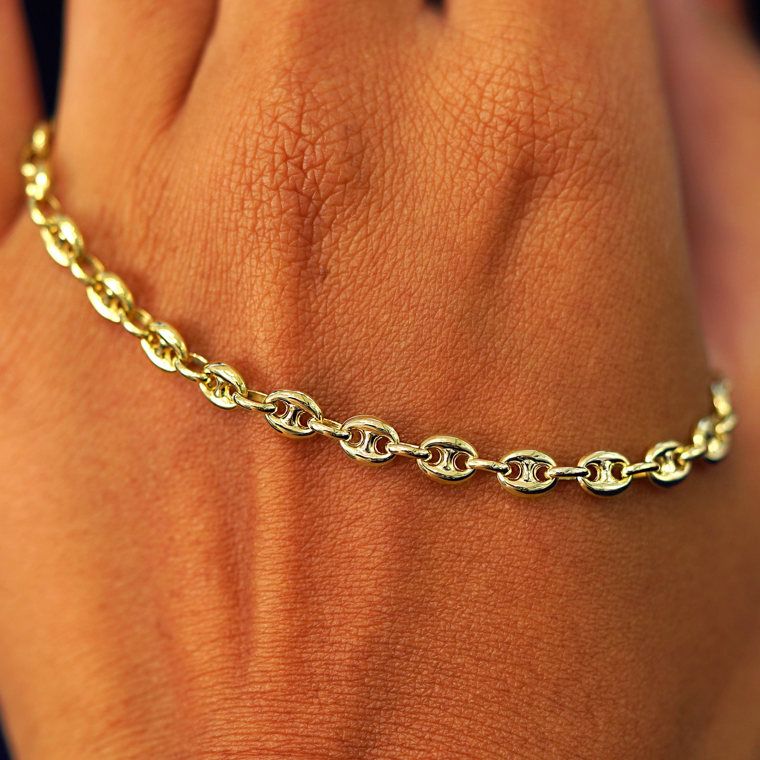 A solid gold Puffy Mariner Chain resting on the back of a model's hand
