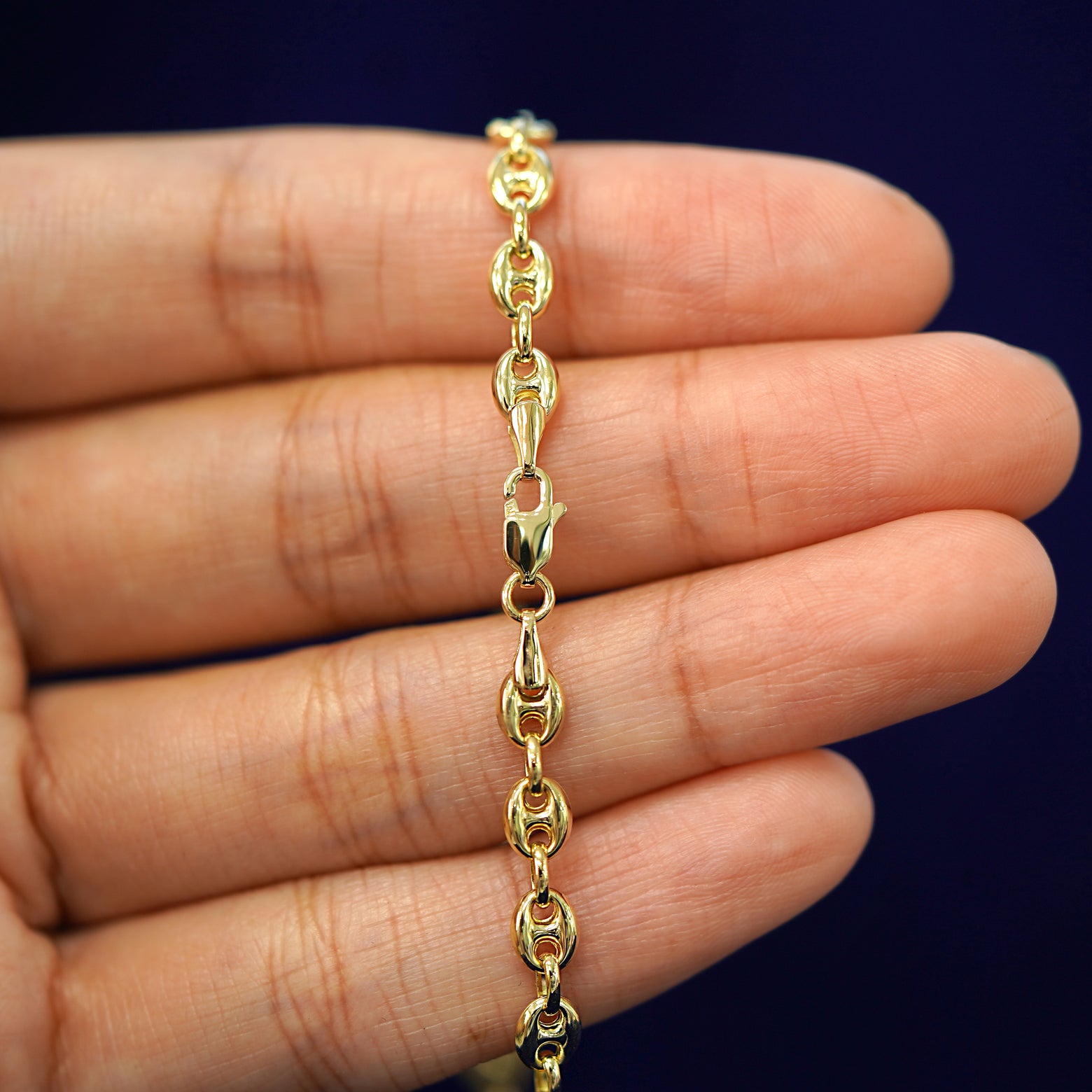 A model's hand holding a yellow 14k gold Puffy Mariner Chain with a lobster claw clasp
