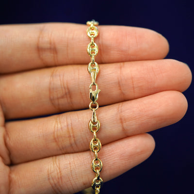 A model's hand holding a yellow 14k gold Puffy Mariner Bracelet with a lobster claw clasp