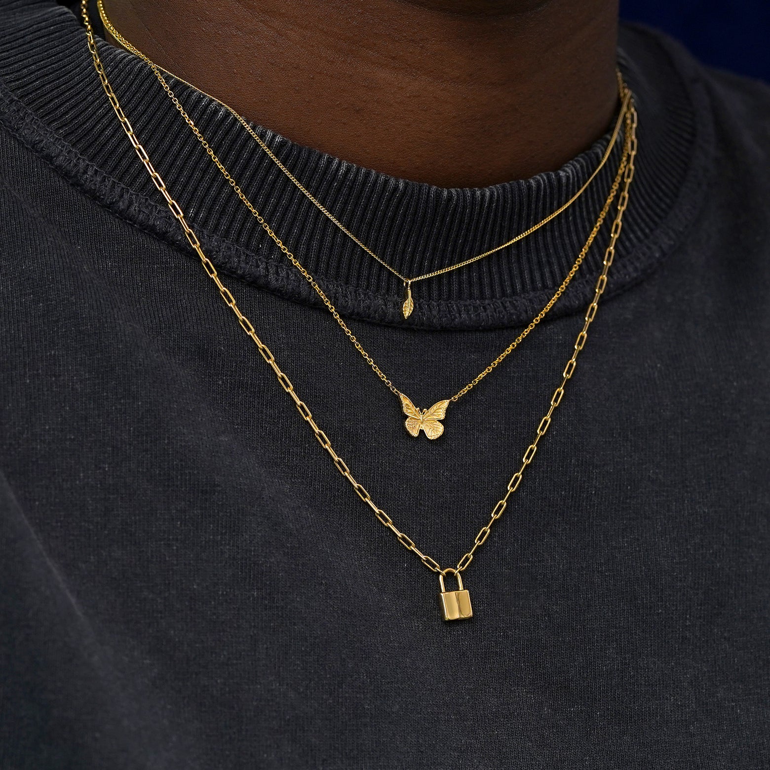 A model wearing solid 14k yellow gold Leaf, Butterfly, and Lock Necklaces layered