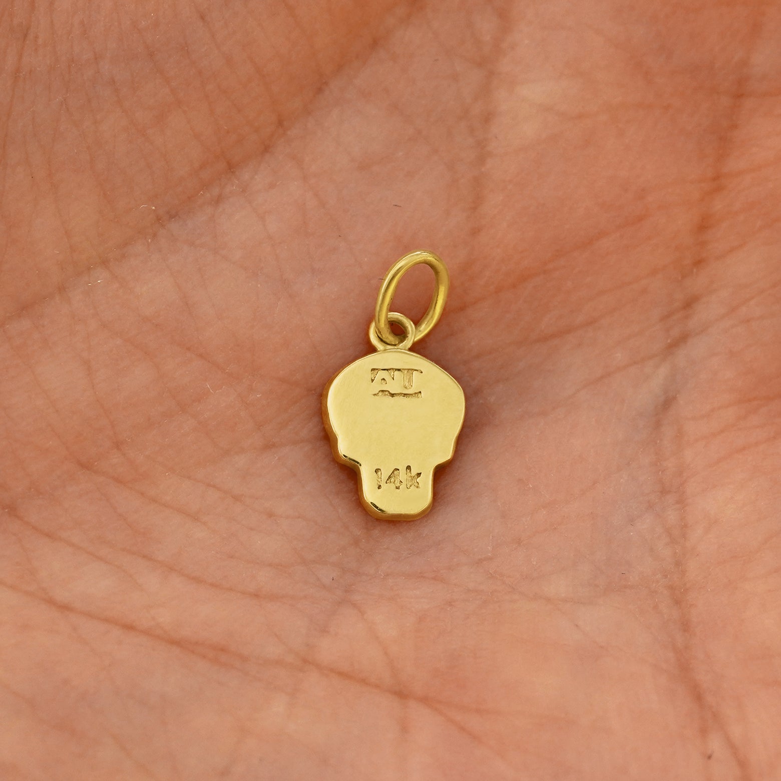 Back view of a solid 14k yellow gold Skull Charm resting on in the palm of a model's hand