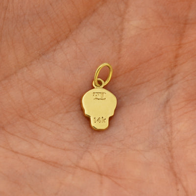 Back view of a solid 14k yellow gold Skull Charm resting on in the palm of a model's hand