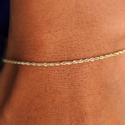 Close up view of a model's wrist wearing a solid 14k yellow gold Rope Bracelet
