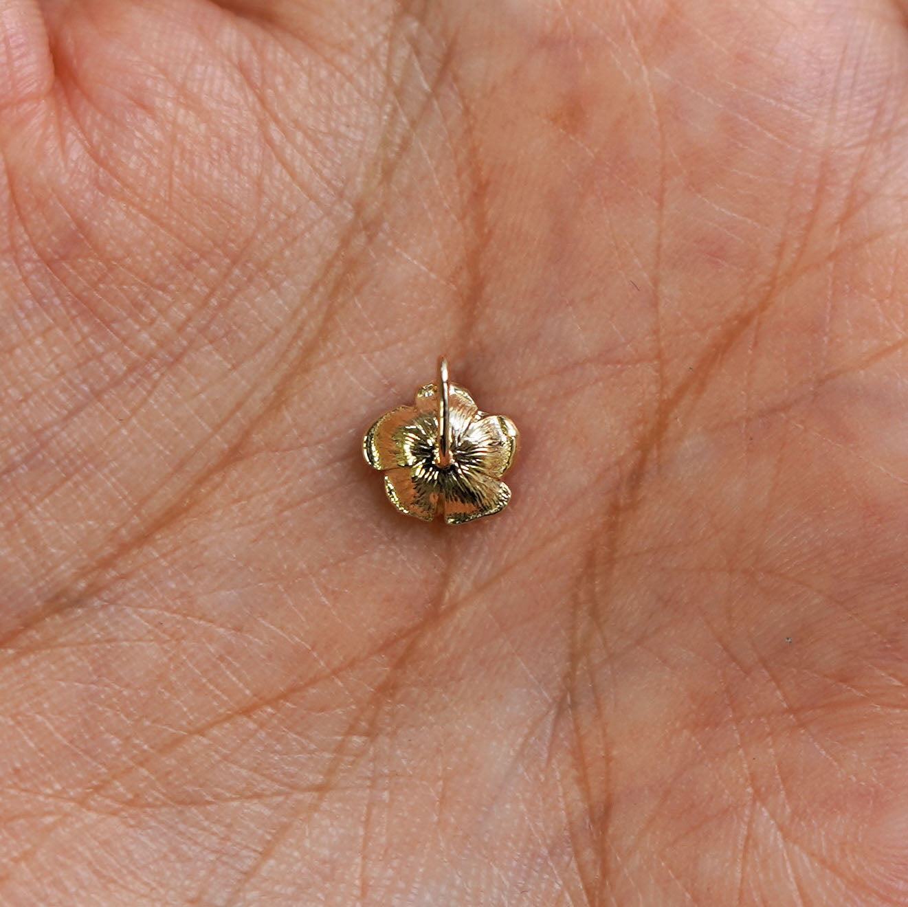 A 14k gold Rose Charm for chain resting in a model's palm to show the underside of the charm