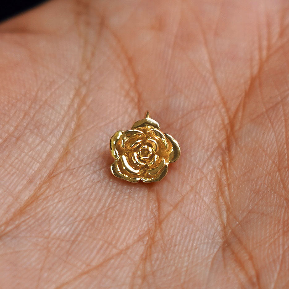 A solid gold Rose Charm for chain resting in a model's palm