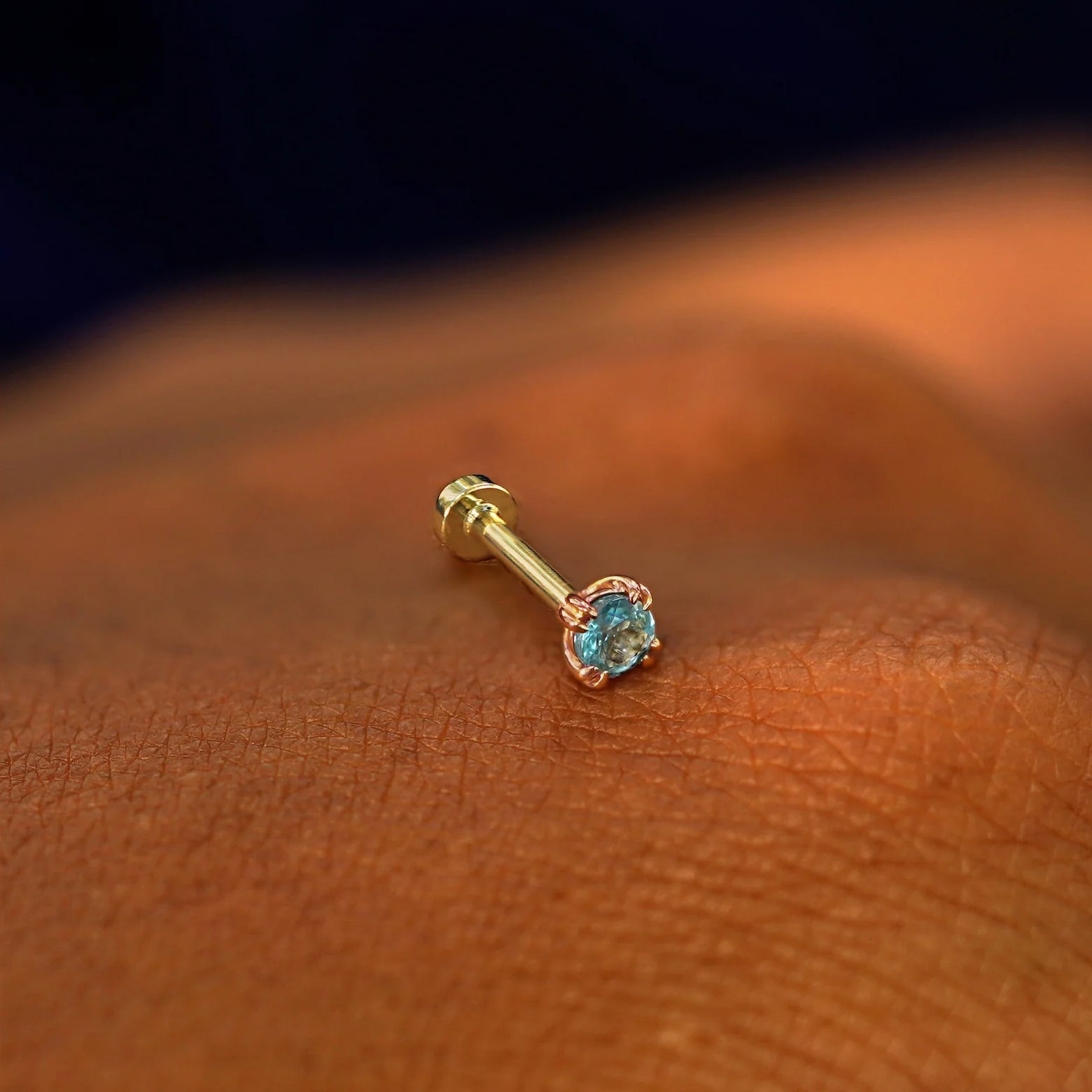 A solid 14k rose gold Aquamarine Flatback Piercing resting on the back of a model's hand