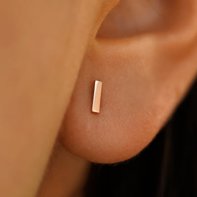 Close up view of a model's ear wearing a 14k rose gold Bar Stud Earring