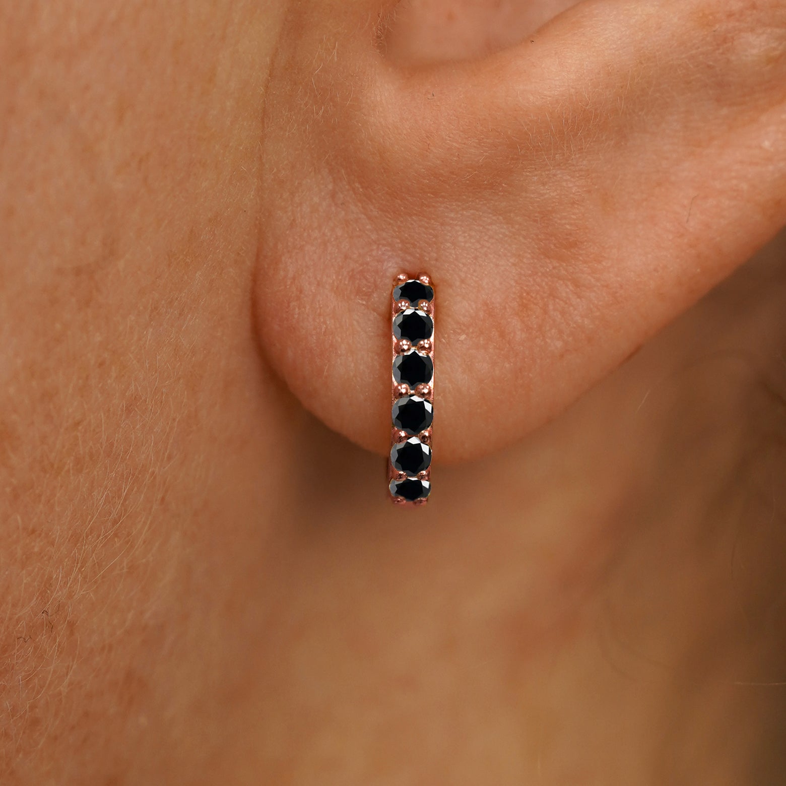Close up view of a model's ear wearing a rose gold Small Black Diamond Huggie Hoop