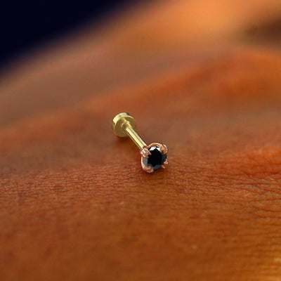 A solid 14k rose gold Black Diamond Flatback Piercing resting on the back of a model's hand