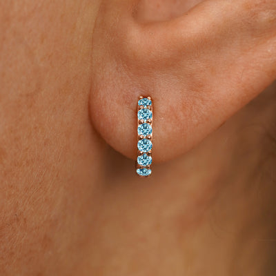 Close up view of a model's ear wearing a rose gold Small Light Blue Lab Diamond Huggie Hoop
