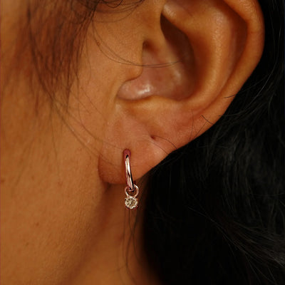 Close up view of a model's ear wearing a rose gold Champagne Diamond Charm on a Curvy Huggie Hoop