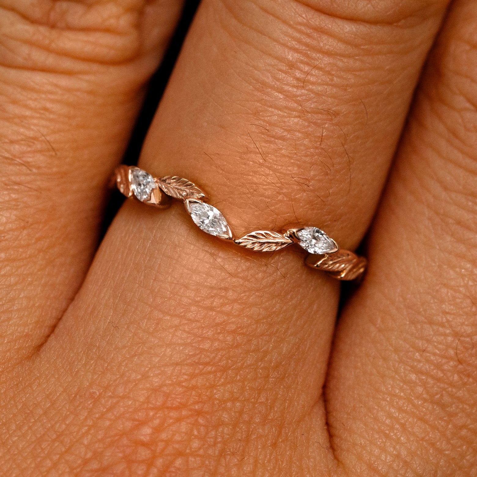 Close up view of a model's fingers wearing a 14k rose gold Chevron Leaves and Marquise Diamonds Band