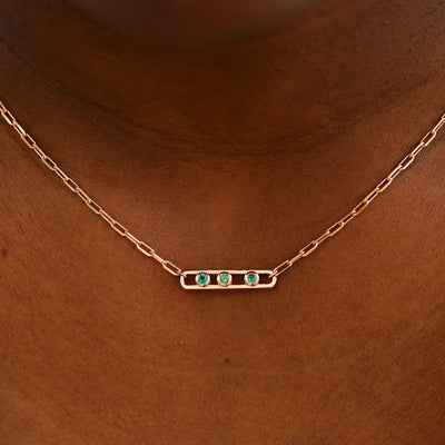Close up view of a model wearing a rose gold Dancing Gemstone necklace with 3 Emeralds