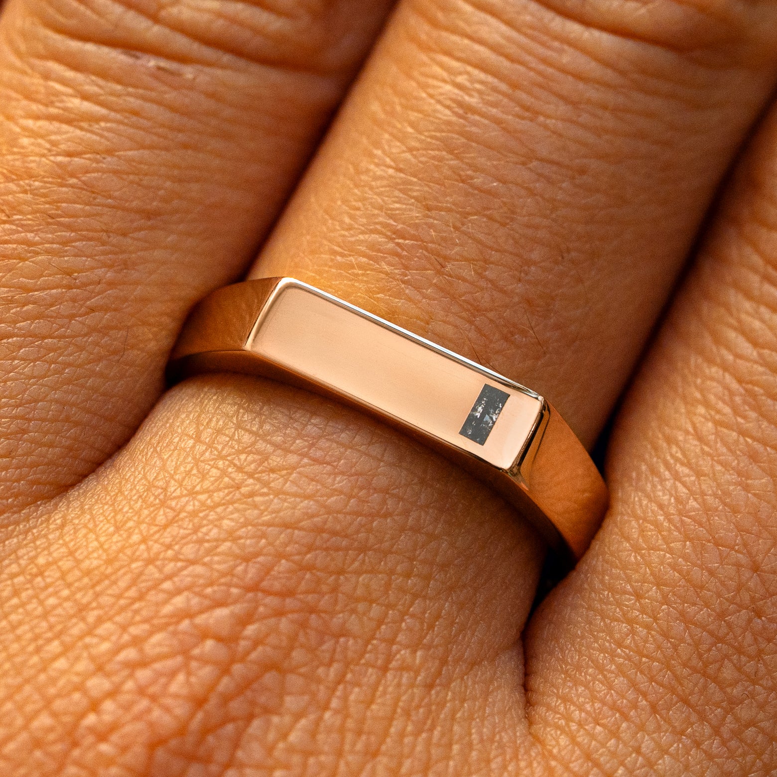 A model's finger wearing a rose gold baguette salt and pepper diamond rectangular signet ring