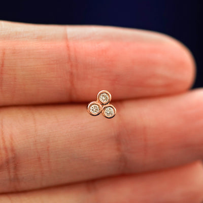 A hand holding a 14k rose gold Diamond Trio stud earring in between their fingers