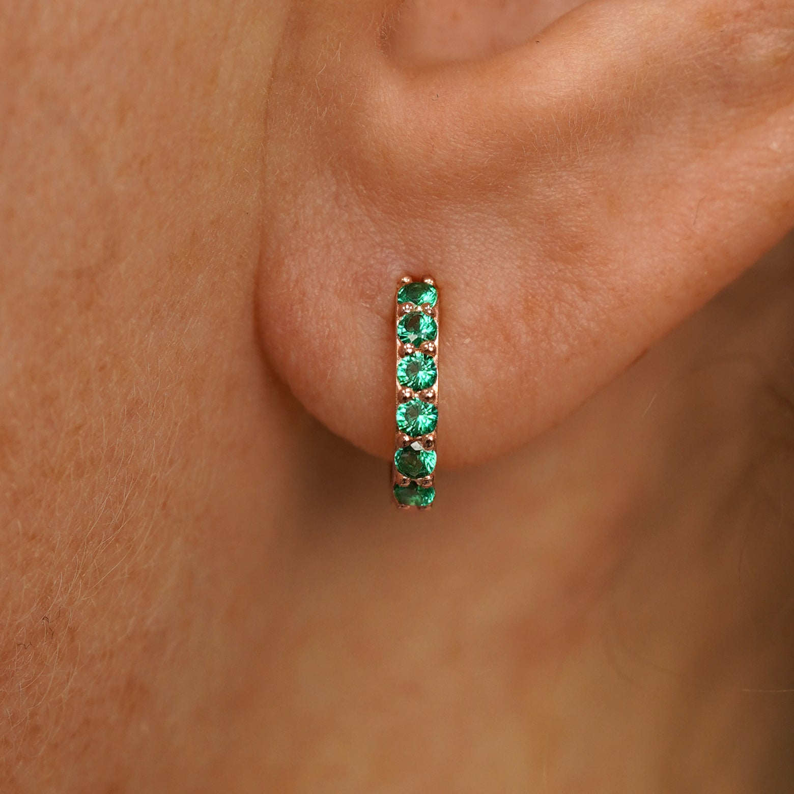 Close up view of a model's ear wearing a rose gold Small Emerald Huggie Hoop