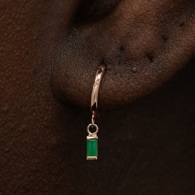 Close up view of a model's ear wearing a rose gold Baguette Emerald Dangle Huggie Hoop