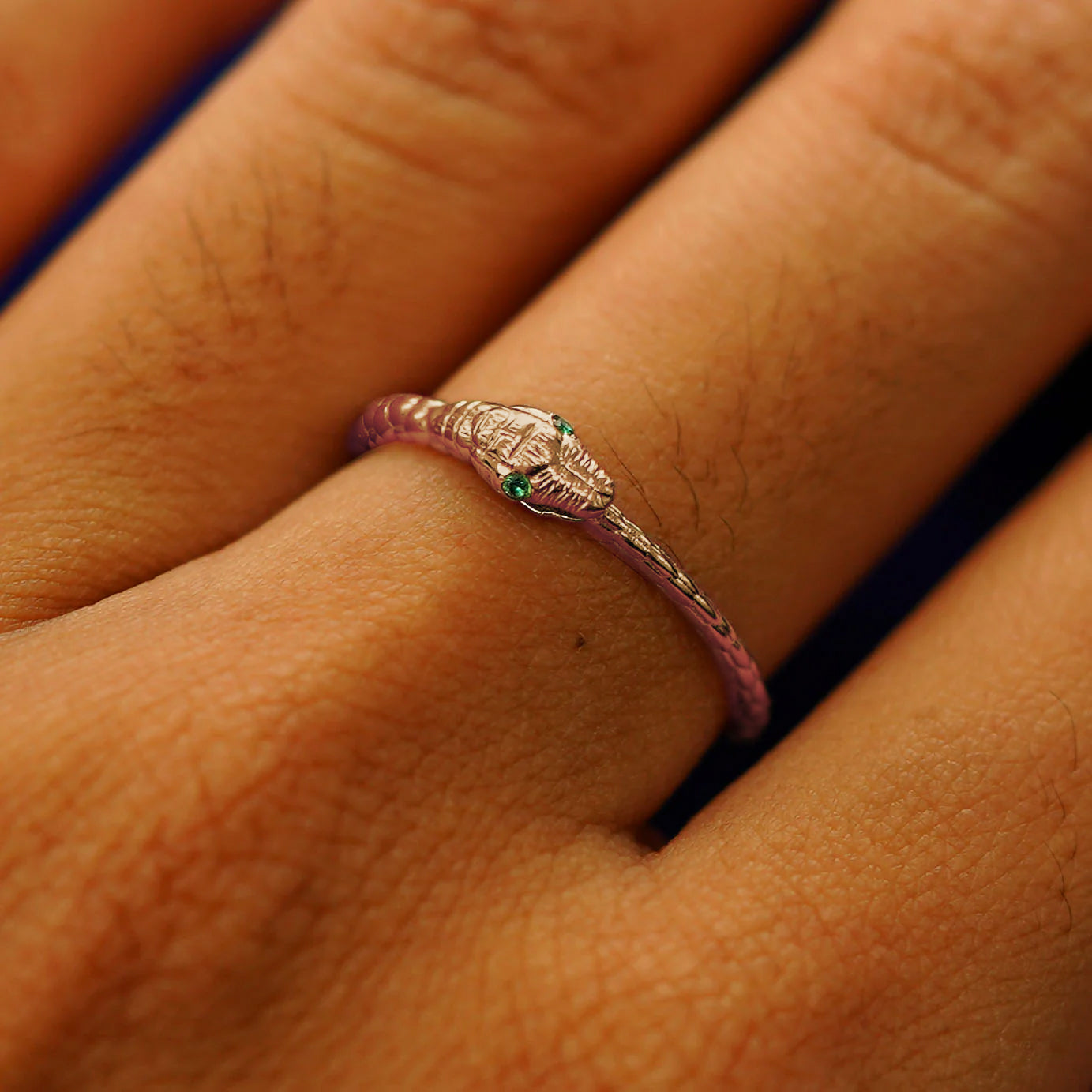Close up view of a model's hand wearing a rose gold emerald Gemstone Ouroboros Snake Ring