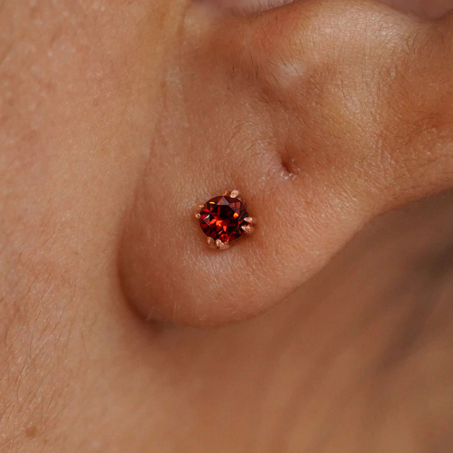 Close up view of a model's ear wearing a 14k rose gold Garnet Earring